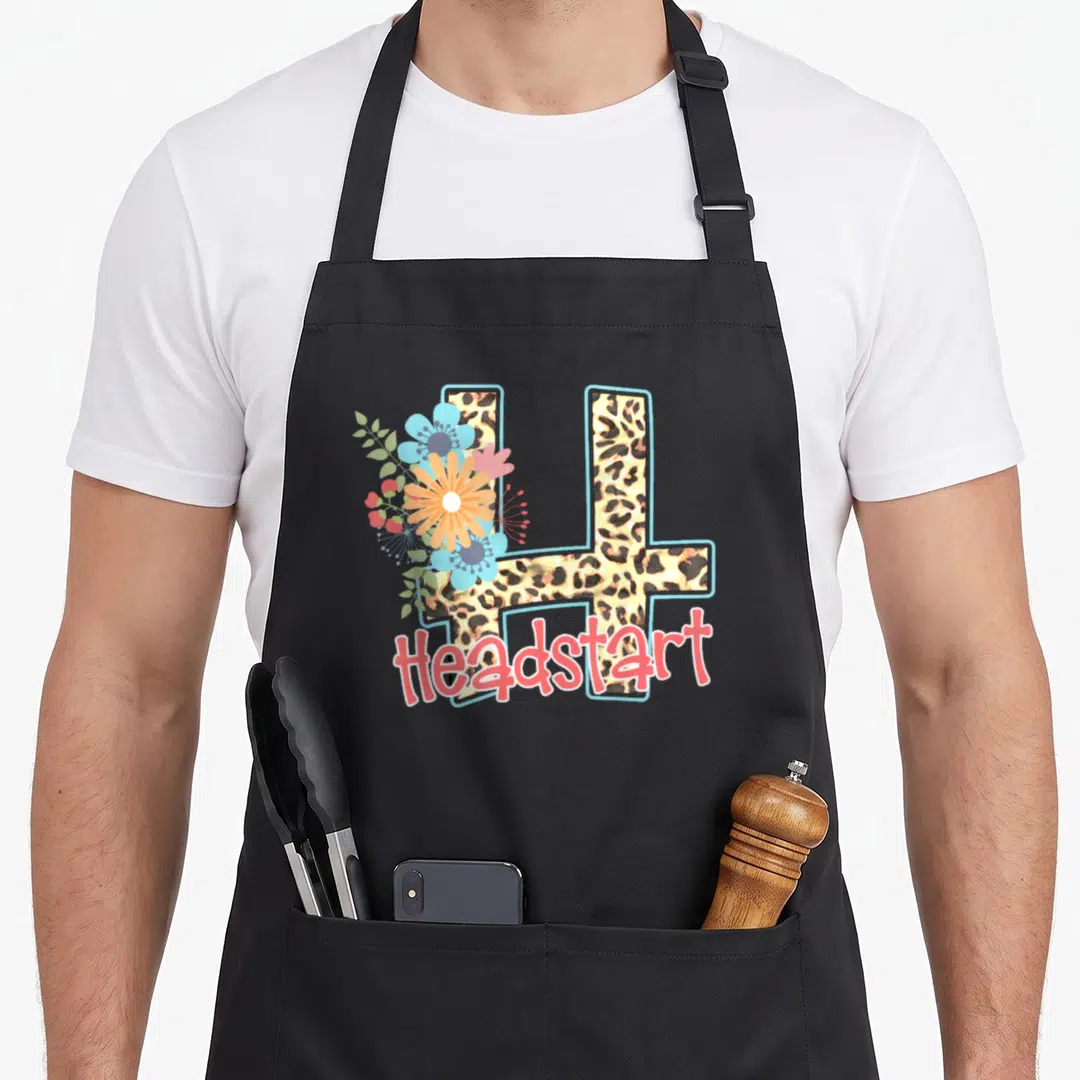 Headstart leopard teacher apron - Leopard print letter H with blue orange and coral flowers and script Headstart text — shown on a black cotton canvas apron against a white background