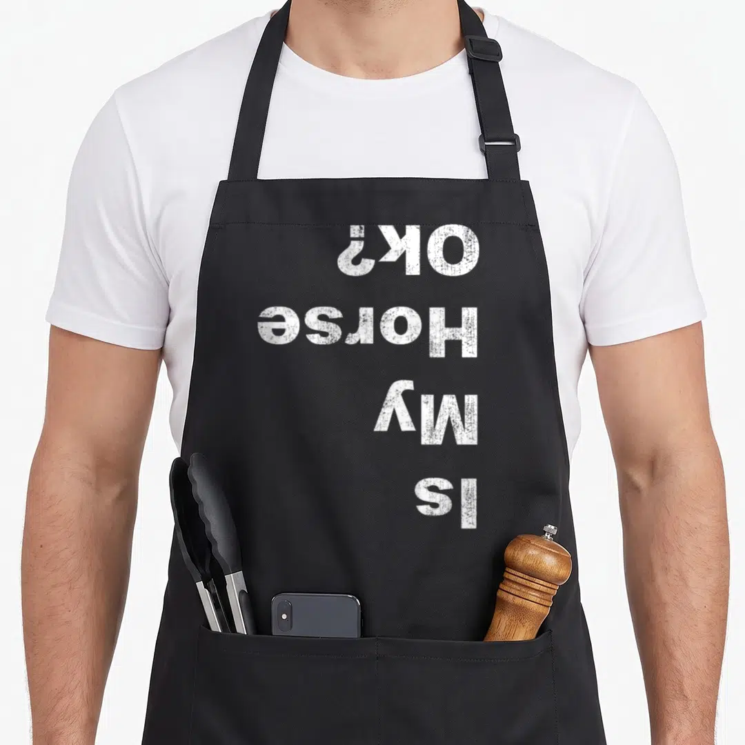 Vintage riding horse apron - White text reading Is My Horse OK printed upside down on black fabric — shown on a black cotton canvas apron against a white background