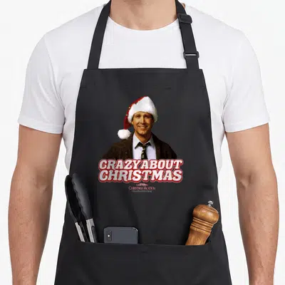 Cute national lampoon's christmas vacation apron - Photo of Clark Griswold in Santa hat with CRAZY ABOUT CHRISTMAS text — shown on a black cotton canvas apron against a white background