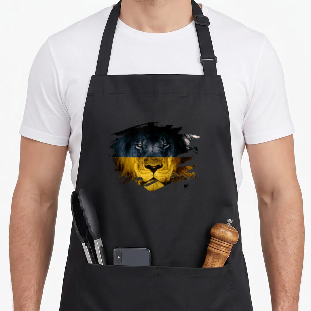 Ukraine african apron - Realistic lion head split horizontally into blue and yellow halves surrounded by black paint — shown on a black cotton canvas apron against a white background