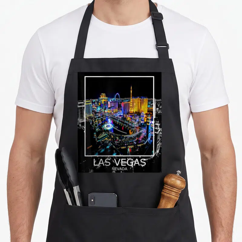 Las lv apron - Framed night photo of Las Vegas skyline with white border and location text below — shown on a black cotton canvas apron against a white background