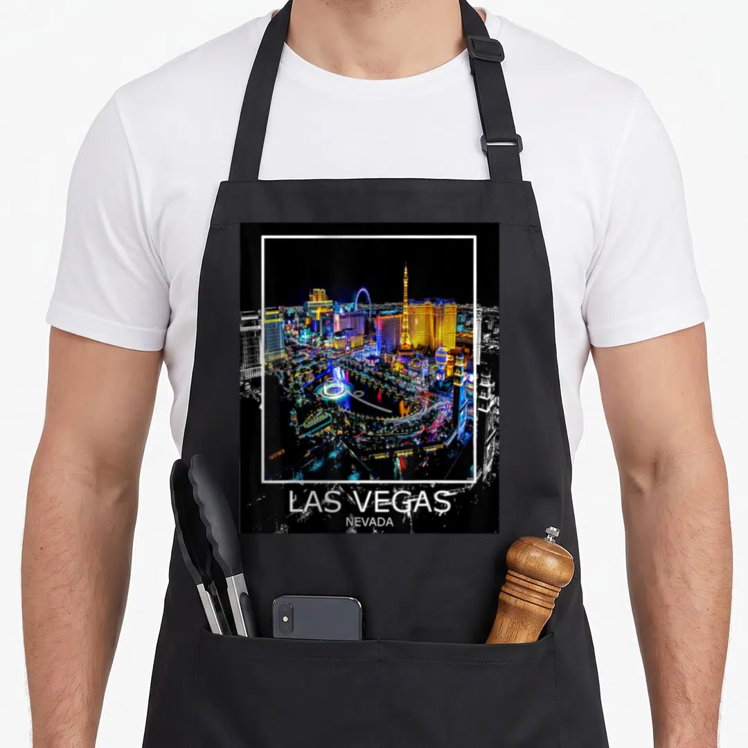 Las lv apron - Framed night photo of Las Vegas skyline with white border and location text below — shown on a black cotton canvas apron against a white background