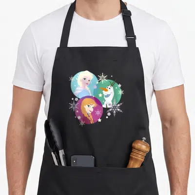 Anna bubble apron - Three cartoon characters in blue magenta and green circles with snowflakes — shown on a black cotton canvas apron against a white background
