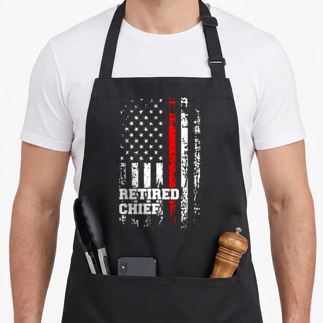 Fire firefighter cooking apron - Distressed flag with red stripe and white retired chief text on black fabric — shown on a black cotton canvas apron against a white background