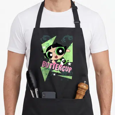 Buttercup cartoon apron - Buttercup character over green triangles and stars with pink text — shown on a black cotton canvas apron against a white background