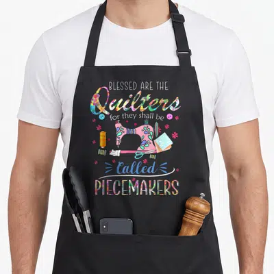 Piecemaker quilter apron - Sewing machine surrounded by colorful thread spools and scissors under stacked text reading — shown on a black cotton canvas apron against a white background