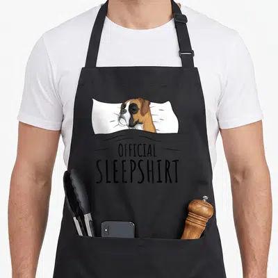 Sleepshirt boxer dog apron - Cartoon boxer dog sleeping on white pillow under grey blanket with stacked text — shown on a black cotton canvas apron against a white background