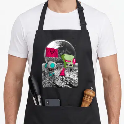 Invader little miss apron - Two cartoon aliens on moon surface, one holds red flag, green and grey design — shown on a black cotton canvas apron against a white background
