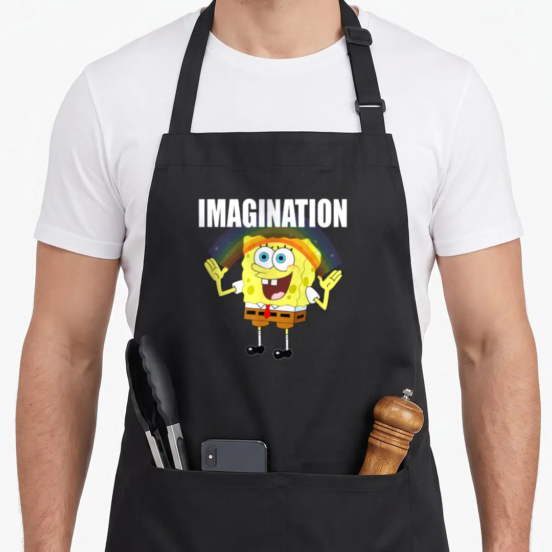 Imagination rainbow apron - SpongeBob SquarePants standing under a rainbow arc with white IMAGINATION text above — shown on a black cotton canvas apron against a white background