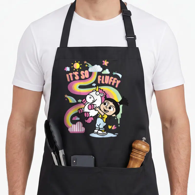 Despicable rainbow apron - Girl hugging unicorn with IT'S SO, FLUFFY text and rainbow background — shown on a black cotton canvas apron against a white background