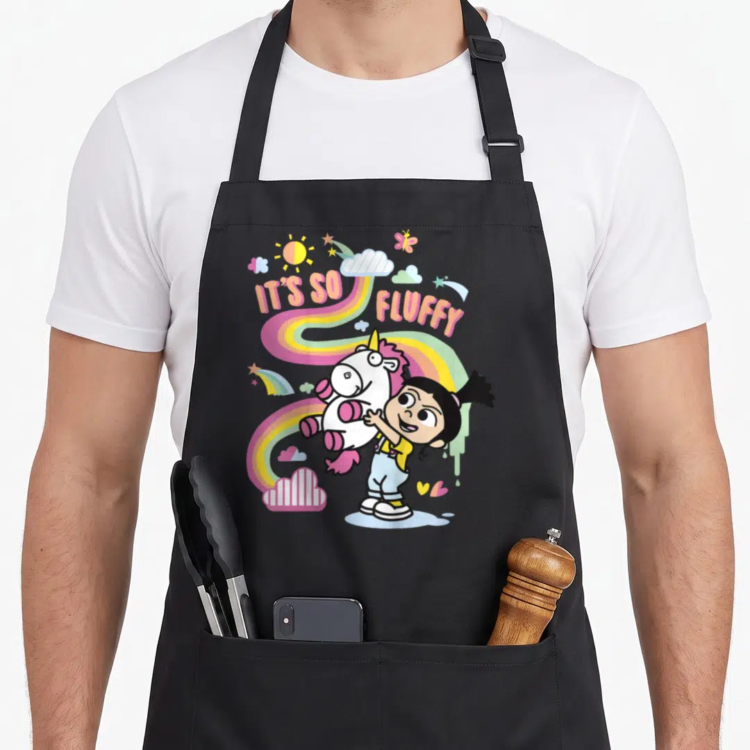 Despicable rainbow apron - Girl hugging unicorn with IT'S SO, FLUFFY text and rainbow background — shown on a black cotton canvas apron against a white background