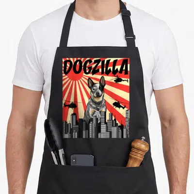 Dogzilla dog kitchen apron - Retro red sunburst poster with giant dog, three helicopters, and city skyline — shown on a black cotton canvas apron against a white background