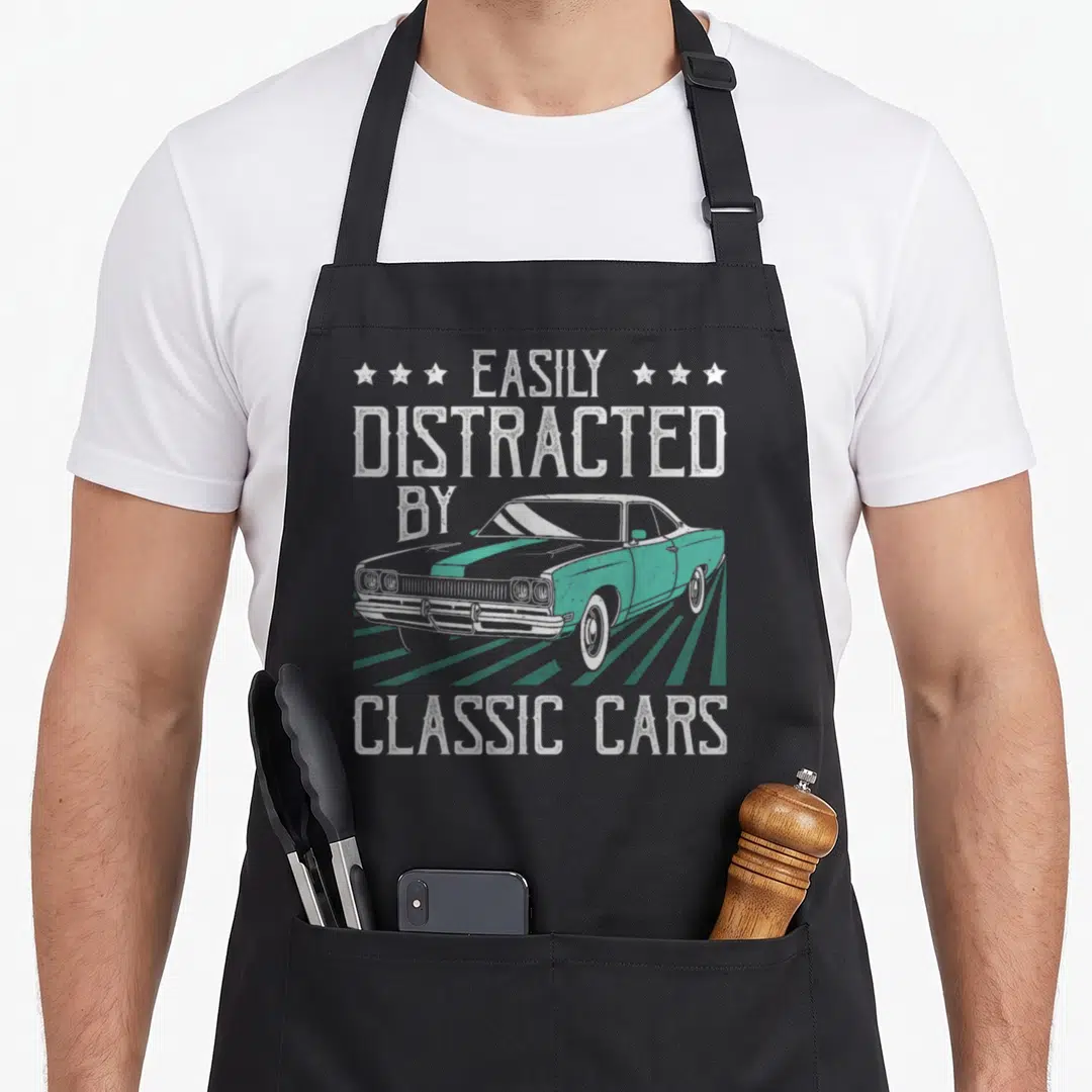 Cute easily car apron - EASILY DISTRACTED BY CLASSIC CARS text with teal vintage car and three stars on each side — shown on a black cotton canvas apron against a white background