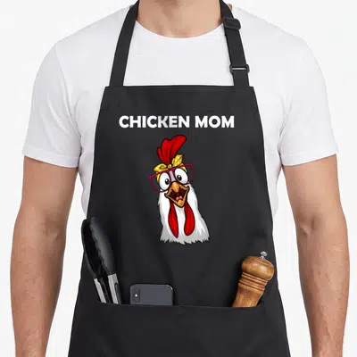 Retro farmer chicken apron - Cartoon white chicken with pink glasses and yellow headband below CHICKEN MOM text — shown on a black cotton canvas apron against a white background