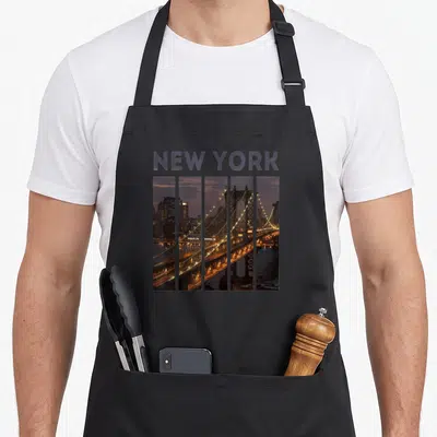 North new york apron - NEW YORK text above five-panel bridge photo in purple, gold, and dark blue — shown on a black cotton canvas apron against a white background