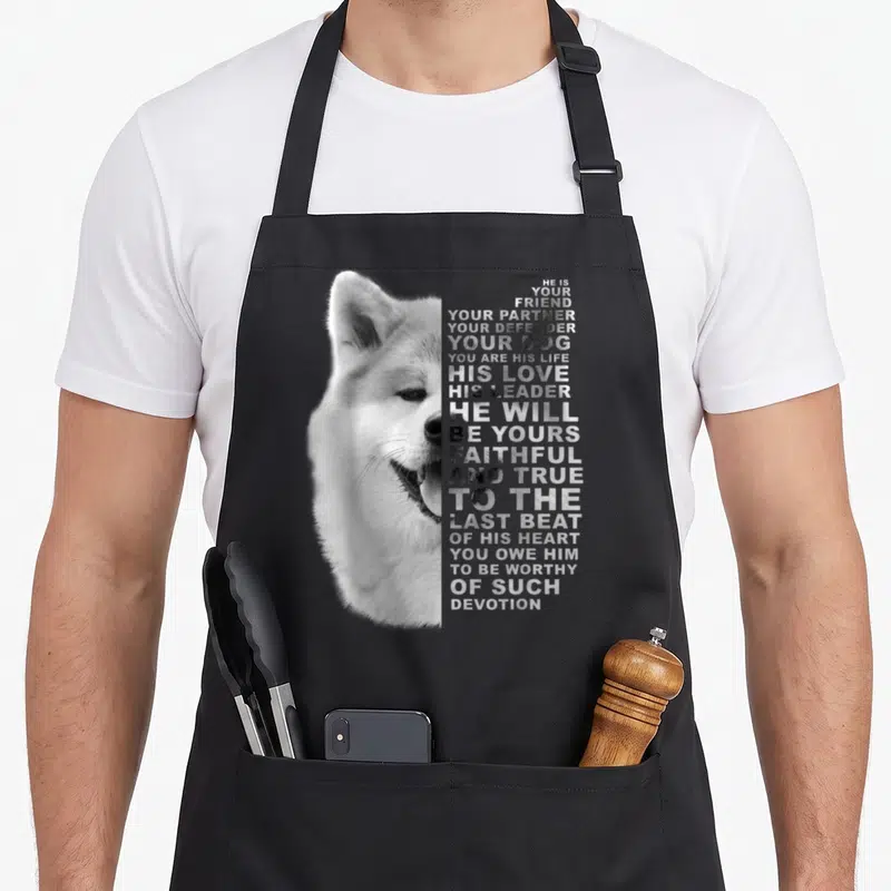 Friend partner dog apron - Black and white Akita Inu head next to stacked text about loyalty and devotion — shown on a black cotton canvas apron against a white background