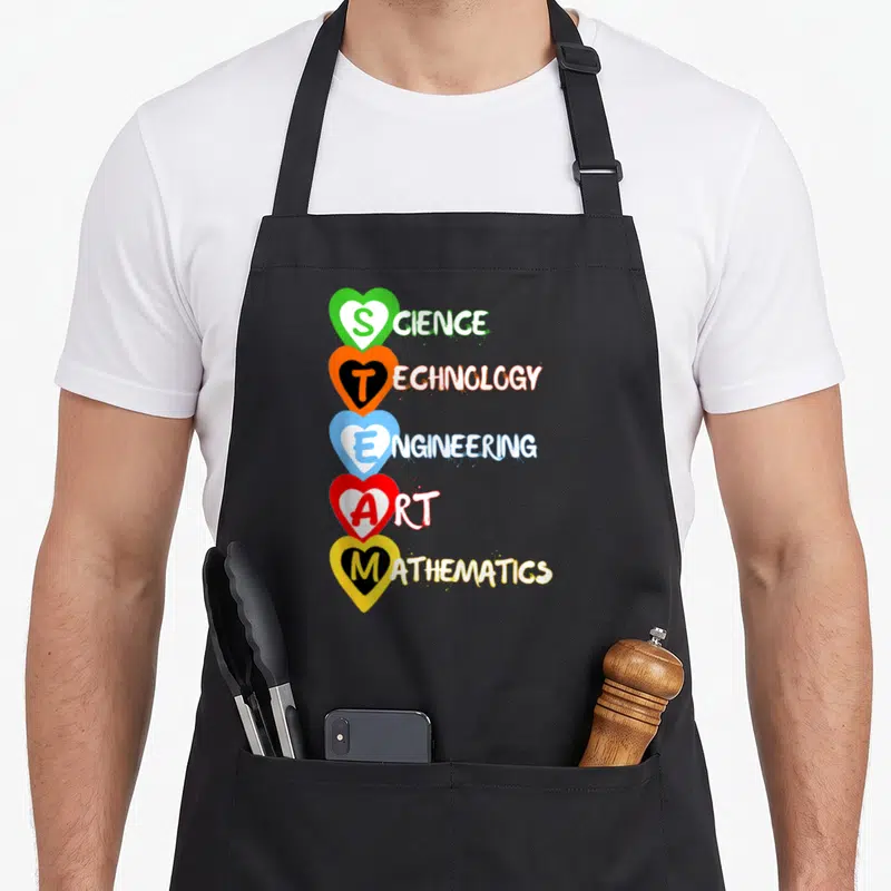 Technical science apron - Five stacked hearts in green orange blue red yellow containing STEAM letters and full words — shown on a black cotton canvas apron against a white background