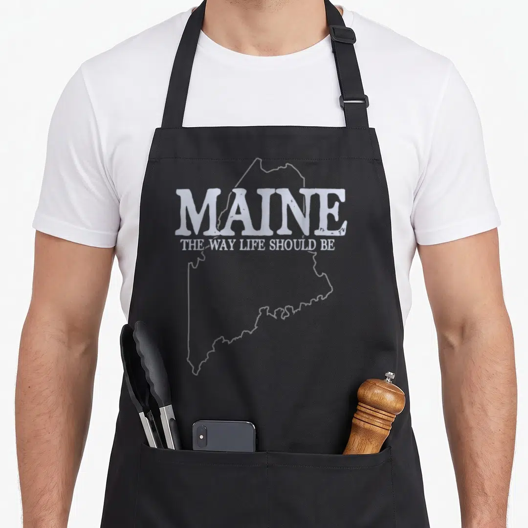 Maine pride apron - White Maine state outline with slogan MAINE THE WAY LIFE SHOULD BE — shown on a black cotton canvas apron against a white background