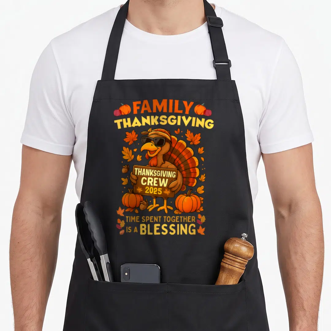 Crew thanksgiving aprons - Cartoon turkey with sunglasses holding 2025 sign surrounded by pumpkins and autumn leaves — shown on a black cotton canvas apron against a white background