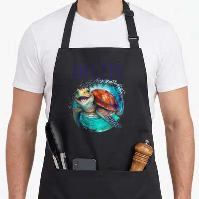 Destin watercolor florida apron - Smiling sea turtle in watercolor splash with DESTIN and FLORIDA text in purple — shown on a black cotton canvas apron against a white background