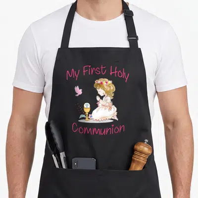 Holy communion aprons - Watercolor girl kneeling in prayer next to a chalice and pink bird with My First Holy Communion — shown on a black cotton canvas apron against a white background