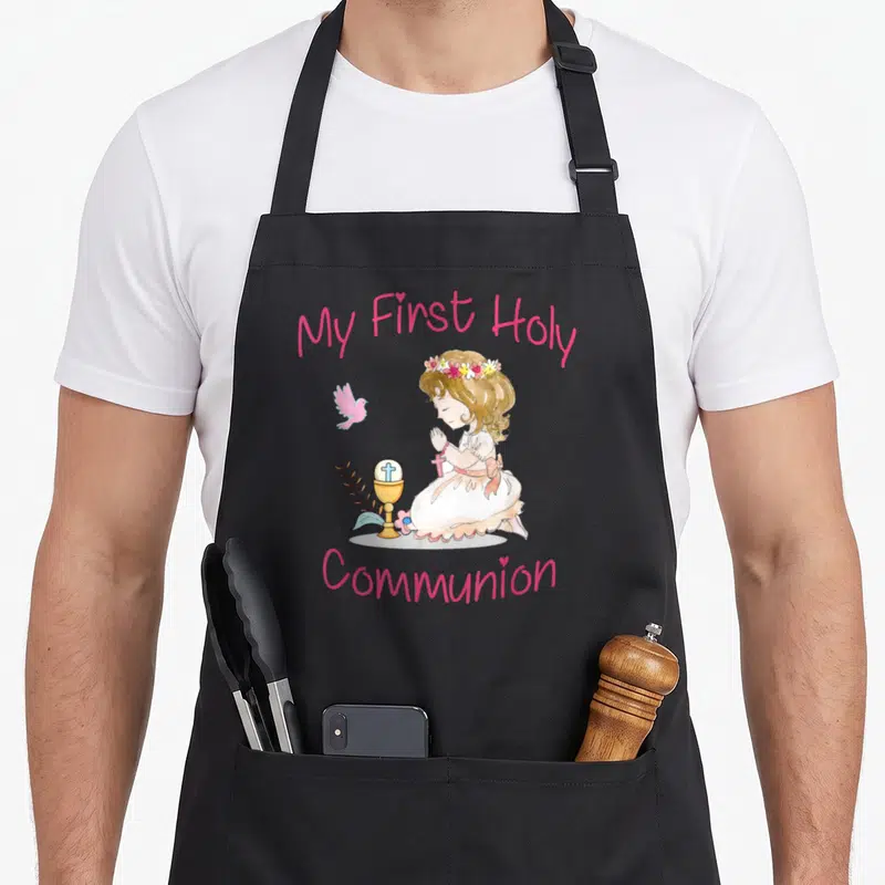 Holy communion aprons - Watercolor girl kneeling in prayer next to a chalice and pink bird with My First Holy Communion — shown on a black cotton canvas apron against a white background