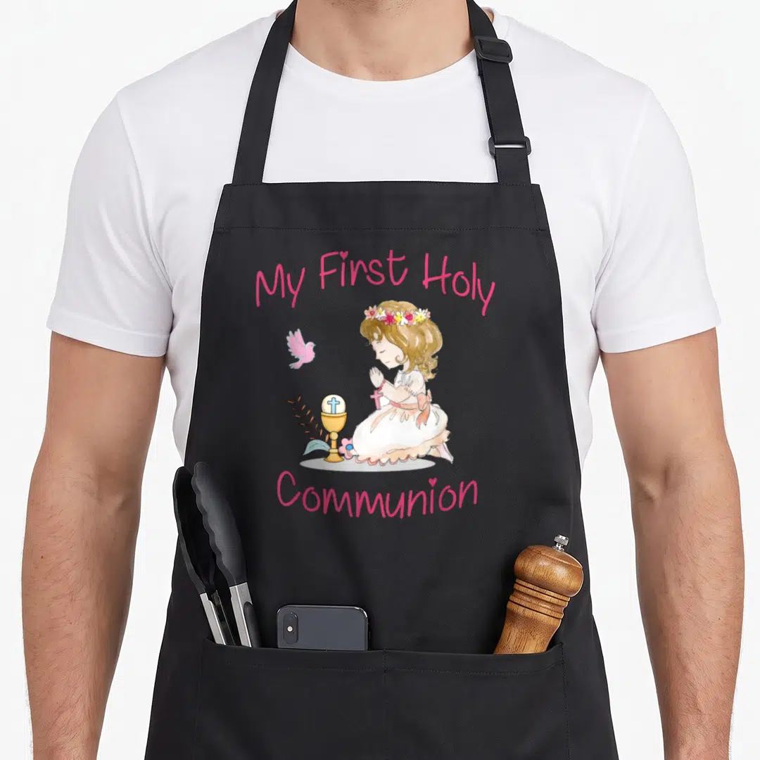 Holy communion aprons - Watercolor girl kneeling in prayer next to a chalice and pink bird with My First Holy Communion — shown on a black cotton canvas apron against a white background