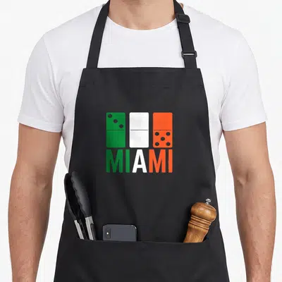 Three zero apron - Three dominoes in green white and orange above MIAMI text — shown on a black cotton canvas apron against a white background
