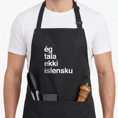 Speak icelandic apron - White text ég tala ekki íslensku stacked vertically on black fabric — shown on a black cotton canvas apron against a white background