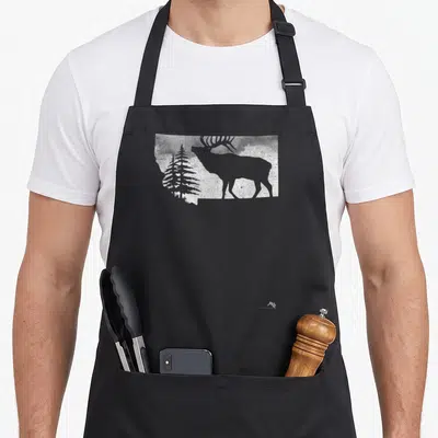 Montana hunter apron - White elk and pine tree silhouette inside a state outline on black fabric — shown on a black cotton canvas apron against a white background