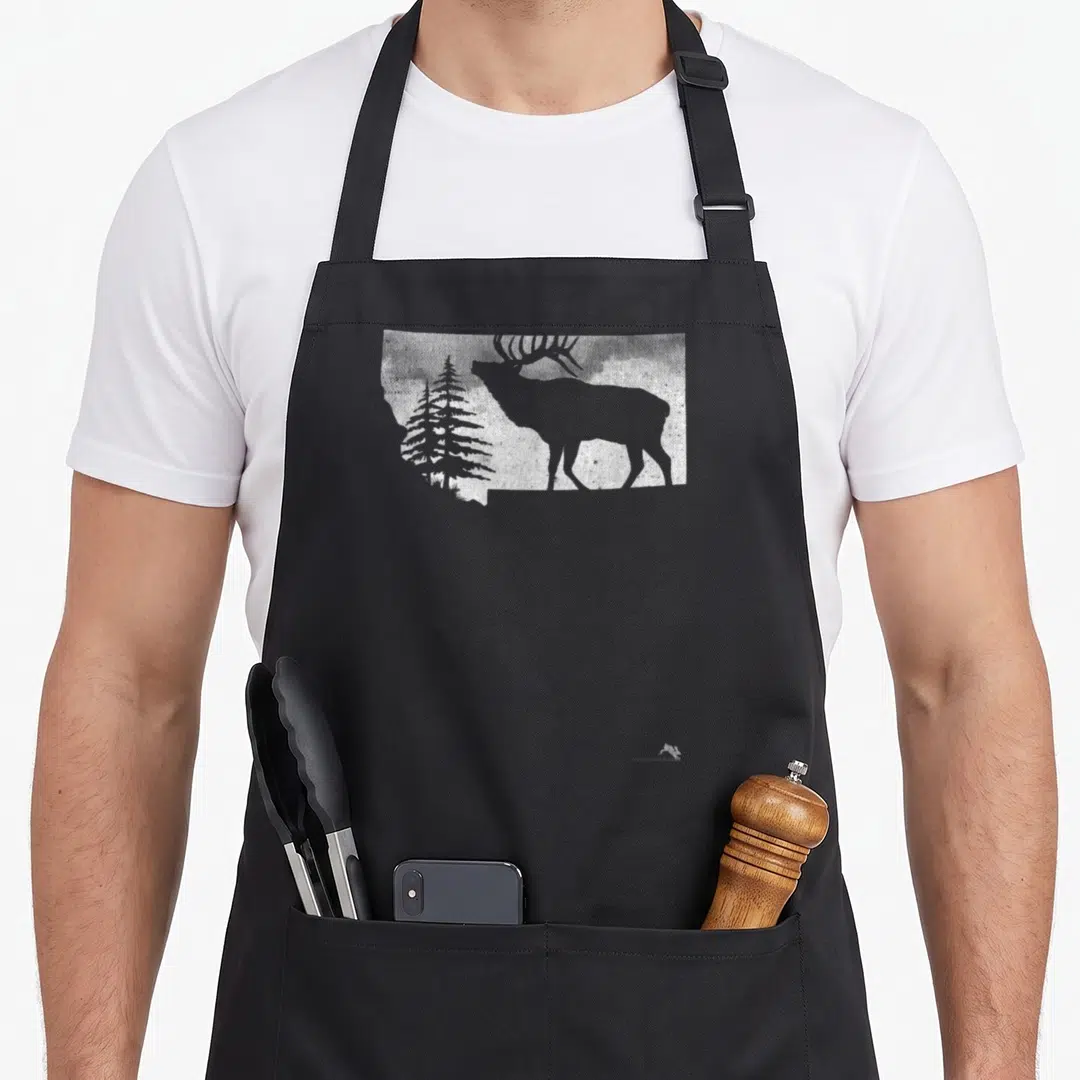 Montana hunter apron - White elk and pine tree silhouette inside a state outline on black fabric — shown on a black cotton canvas apron against a white background