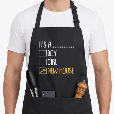 Homeowner modern apron - Yellow key inside checkbox next to NEW HOUSE text below BOY and GIRL options — shown on a black cotton canvas apron against a white background