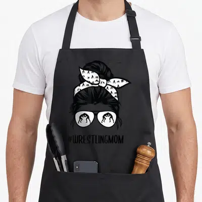 Wrestling bun messy aprons - Stylized woman head with bun and sunglasses containing wrestler silhouettes — shown on a black cotton canvas apron against a white background