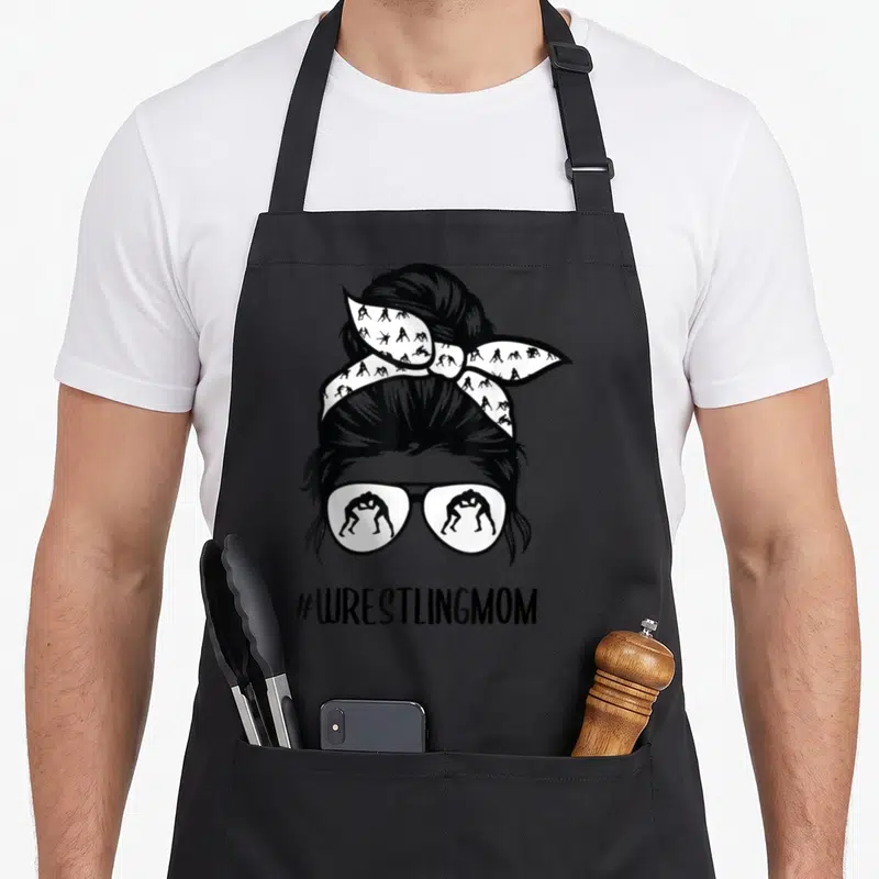 Wrestling bun messy aprons - Stylized woman head with bun and sunglasses containing wrestler silhouettes — shown on a black cotton canvas apron against a white background