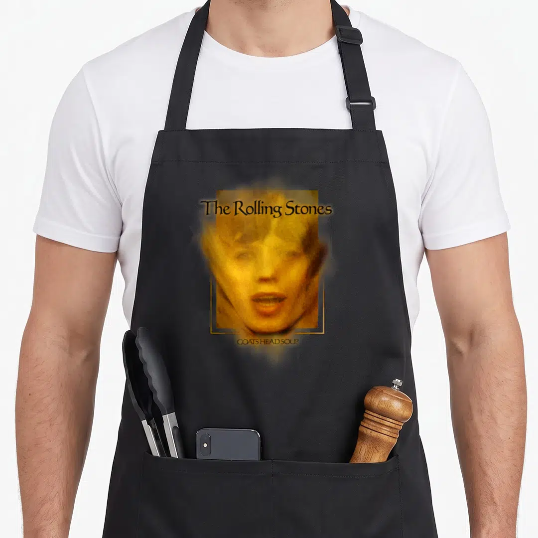 Goat rolling stones apron - Man's face in yellow and orange tones framed by The Rolling Stones and GOATS HEAD SOUP text — shown on a black cotton canvas apron against a white background