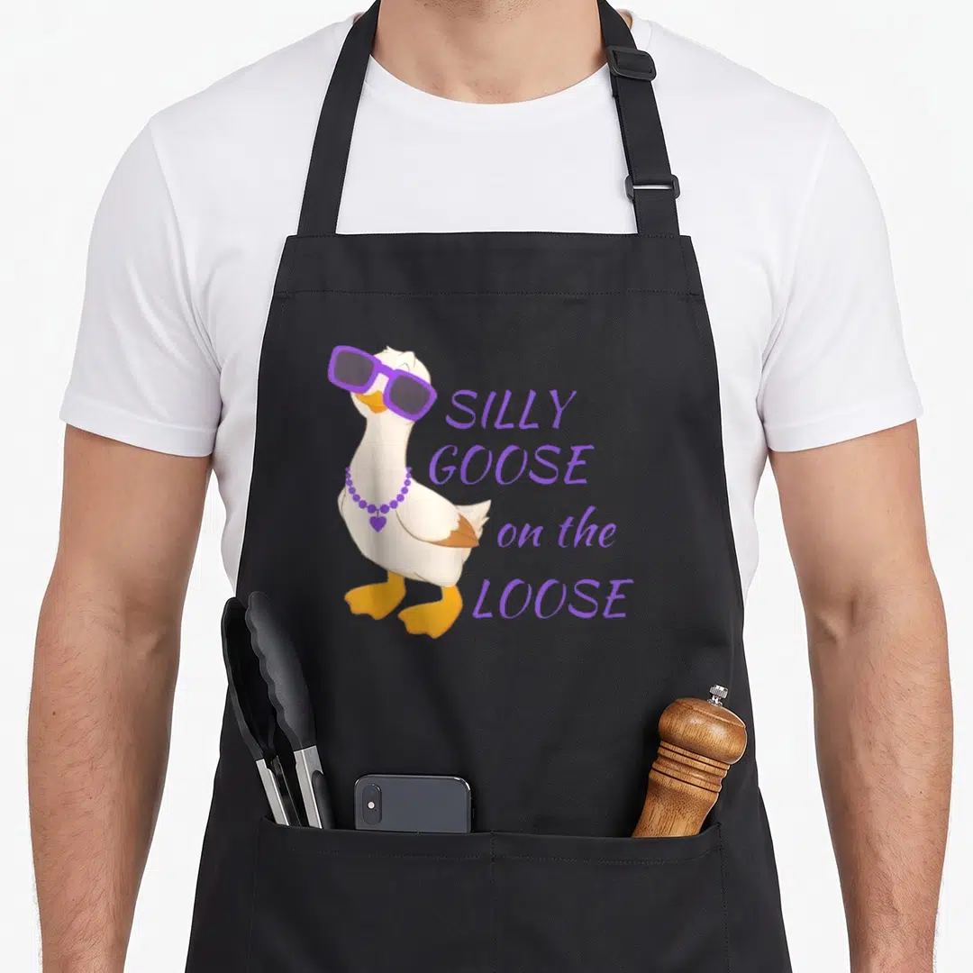 Funny goose silly apron - Cartoon white goose in purple sunglasses and necklace beside stacked purple text — shown on a black cotton canvas apron against a white background