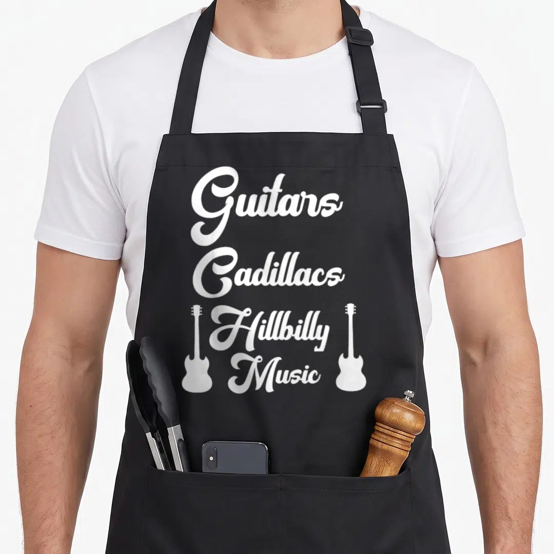 Hillbilly music cook's country aprons - White stacked text Guitars Cadillacs Hillbilly Music flanked by two guitar — shown on a black cotton canvas apron against a white background