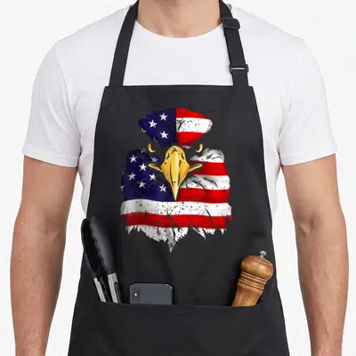 Eagle flag 4th of july apron - Realistic eagle head filled with red white and blue stars and stripes pattern — shown on a black cotton canvas apron against a white background
