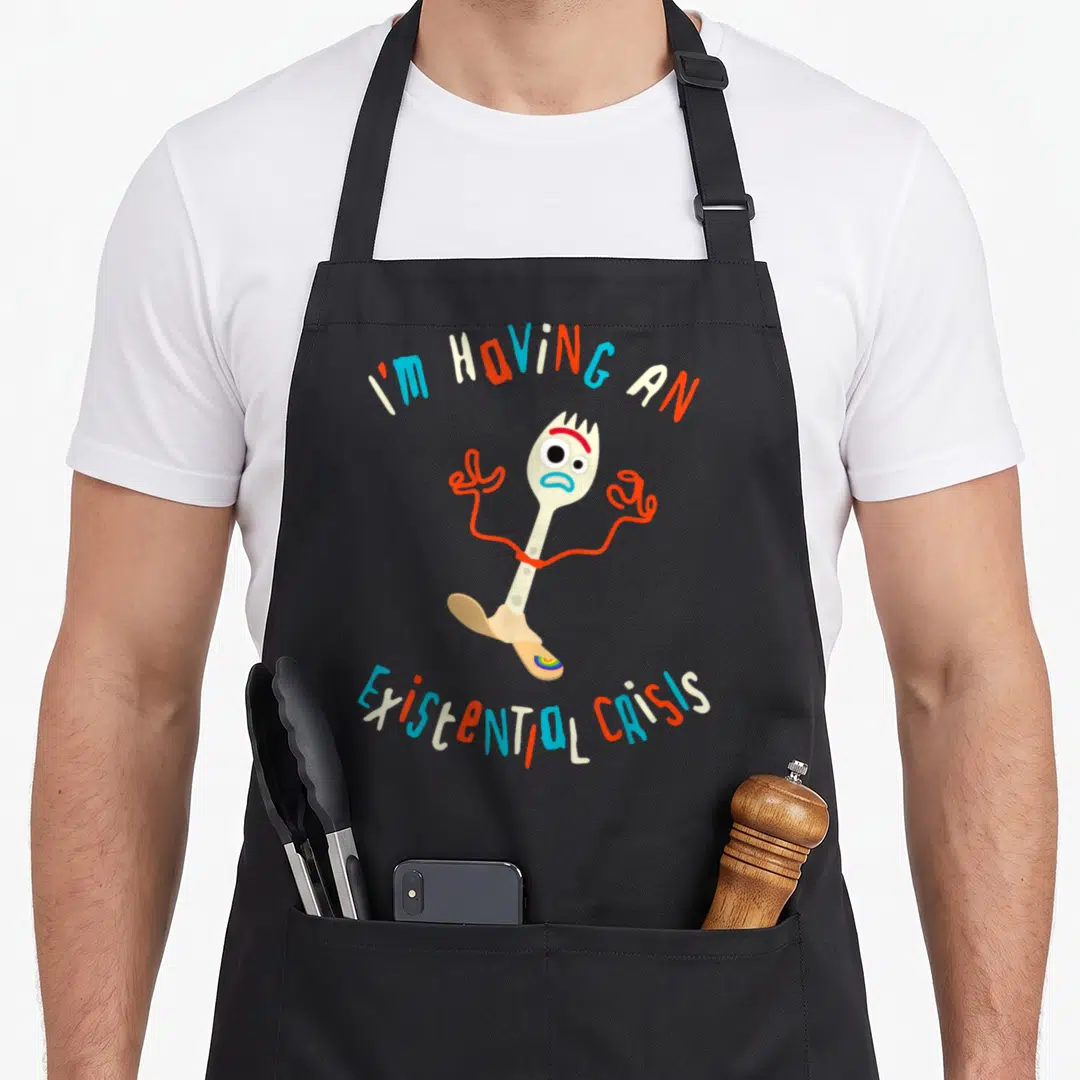 Existential dog breed aprons - Fork character with distressed face between arched text I'M HAVING AN EXISTENTIAL CRISIS — shown on a black cotton canvas apron against a white background