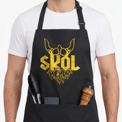 Skol viking apron - Yellow distressed viking face formed by SKOL text with horns and beard — shown on a black cotton canvas apron against a white background