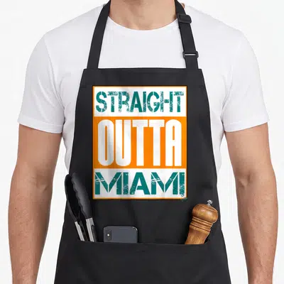 Miami hip apron - STRAIGHT OUTTA MIAMI text in teal and white on orange and white stacked blocks — shown on a black cotton canvas apron against a white background