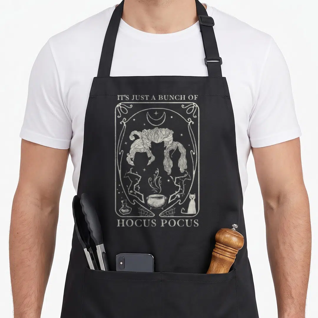 Bunch sister apron - White line art of witch hair, cauldron, and cat with Hocus Pocus text on black apron — shown on a black cotton canvas apron against a white background