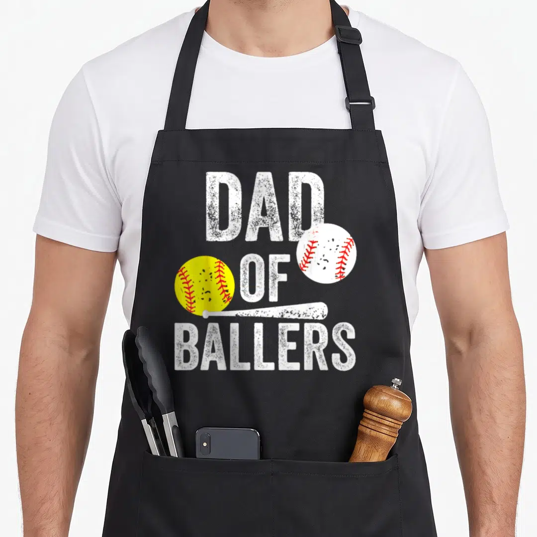 Baller baseball apron - Dad of Ballers text with yellow softball, white baseball, and bat in distressed white, yellow — shown on a black cotton canvas apron against a white background