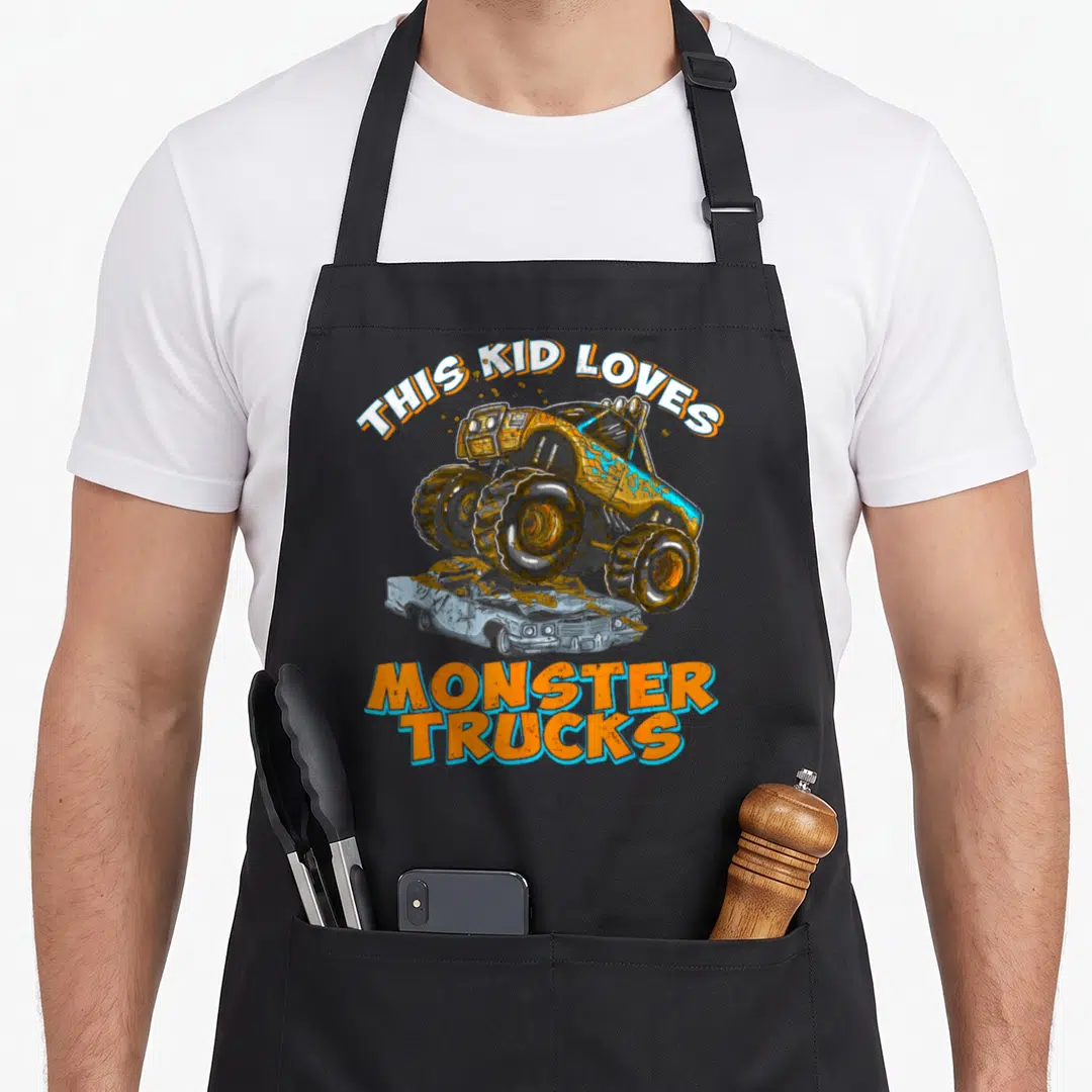 Monster pickup truck apron - THIS KID LOVES MONSTER TRUCKS text with orange and blue truck crushing silver car — shown on a black cotton canvas apron against a white background