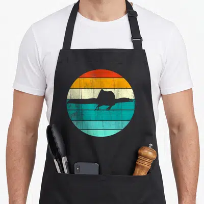 Spinosaurus sunset dinosaur apron - Grey swimming Spinosaurus silhouette over red orange yellow teal retro stripes — shown on a black cotton canvas apron against a white background