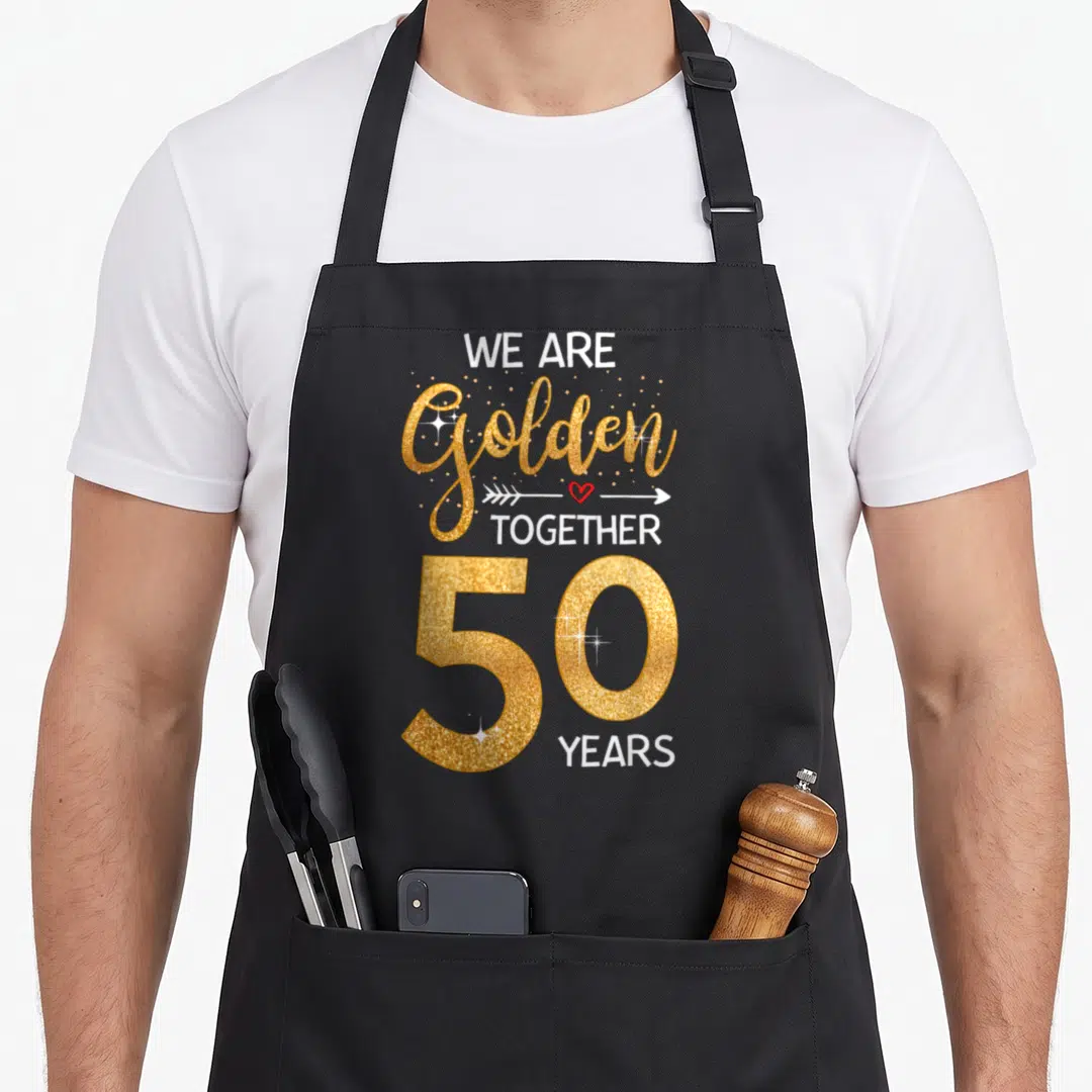 Together wedding aprons - WE ARE golden TOGETHER 50 YEARS text with red heart arrow and gold glitter effect — shown on a black cotton canvas apron against a white background