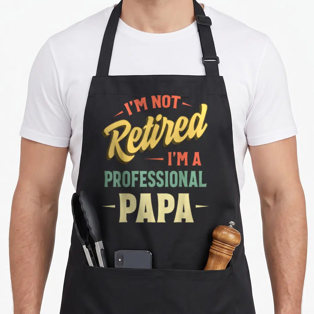 Papa professional apron - Stacked typography I'm Not Retired I'm A Professional Papa in yellow orange green — shown on a black cotton canvas apron against a white background