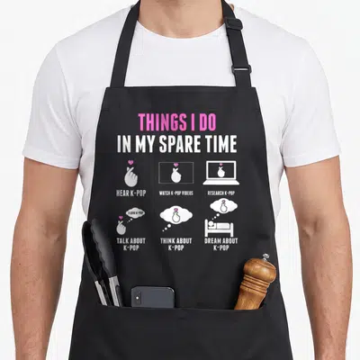 Pop spare time apron - White and pink text listing k-pop activities with hand gesture icons — shown on a black cotton canvas apron against a white background