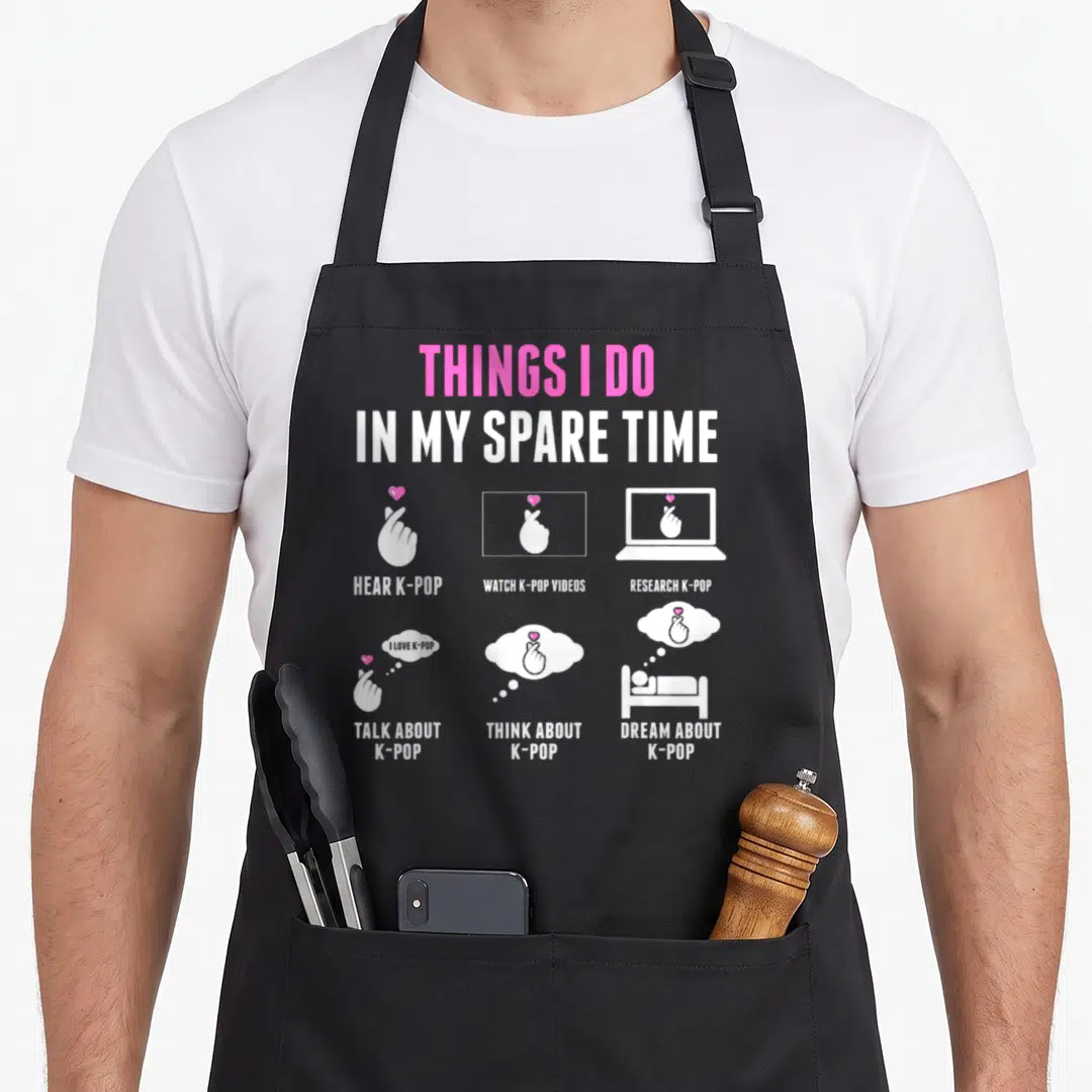 Pop spare time apron - White and pink text listing k-pop activities with hand gesture icons — shown on a black cotton canvas apron against a white background