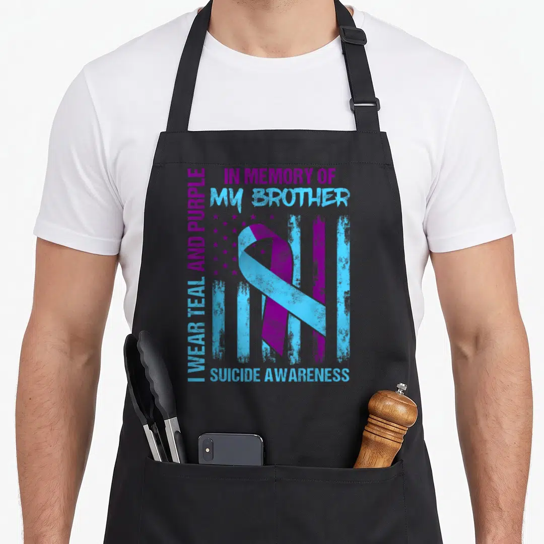 Brother ribbon apron - Teal and purple ribbon over distressed flag with memory text — shown on a black cotton canvas apron against a white background